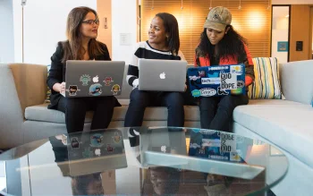 women with their laptops out and laughing on a couch